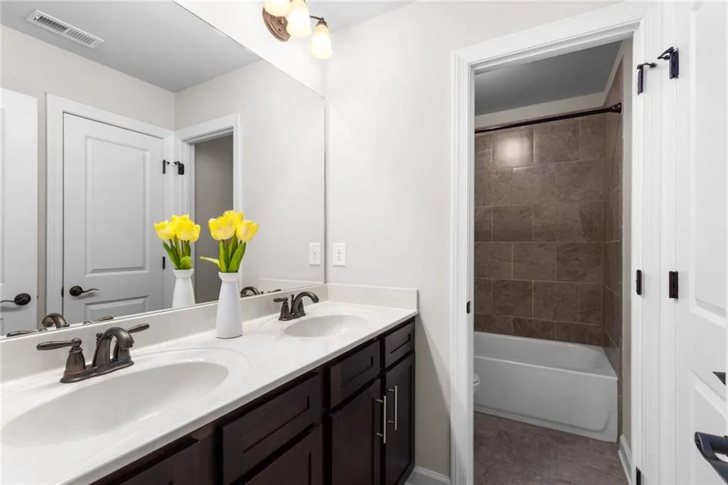 Full bathroom with toilet, tile floors, tiled shower / bath combo, large vanity, and double sink