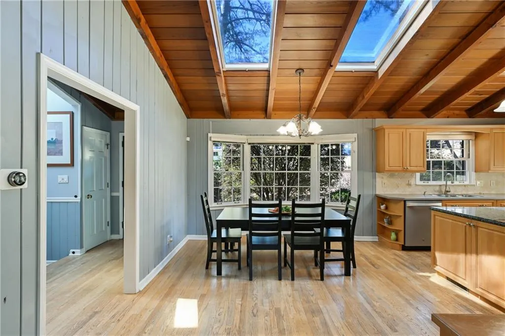 Dining room featuring light wood finished floors, wood ceiling, a chandelier, vaulted ceiling with skylight, and baseboards