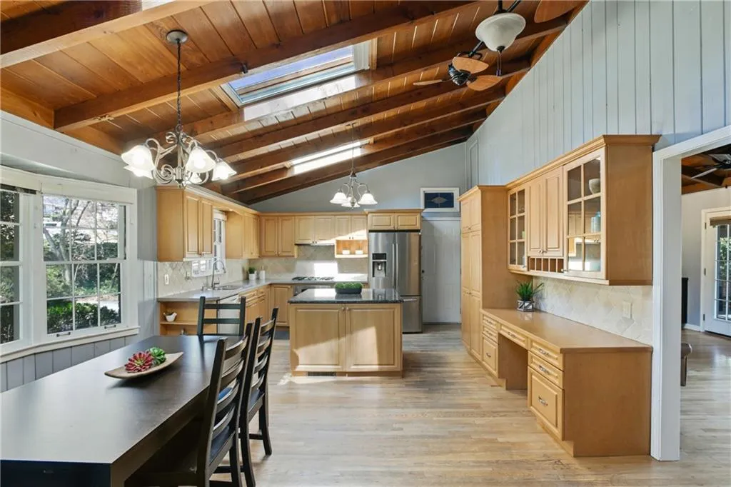 Kitchen with vaulted ceiling with skylight, a notable chandelier, a sink, stainless steel refrigerator with ice dispenser, and backsplash