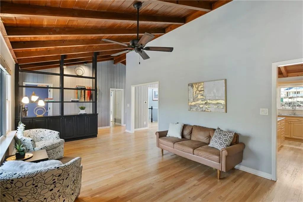 Living area with baseboards, a ceiling fan, wood ceiling, light wood-style floors, and beam ceiling