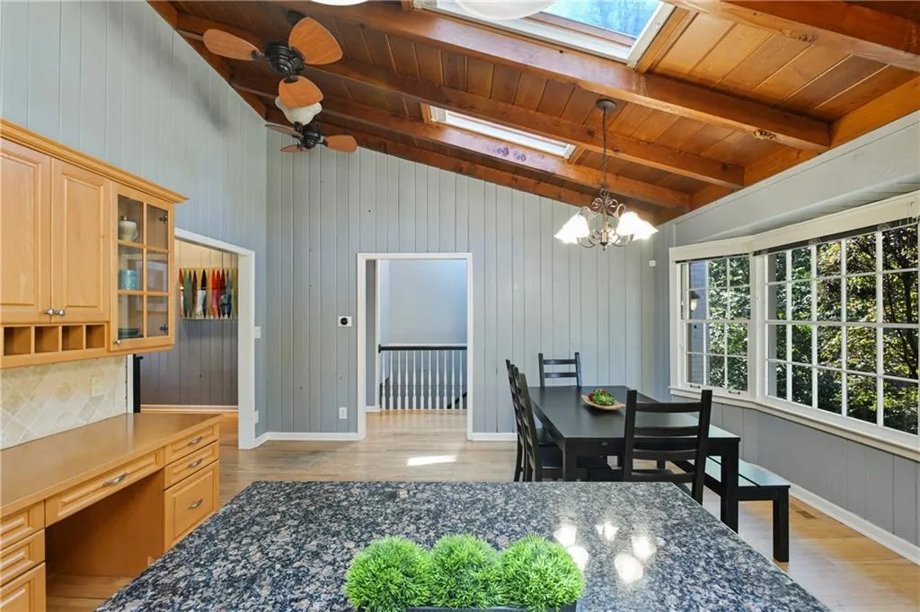 Dining room featuring lofted ceiling with skylight, built in study area, light wood-type flooring, wooden ceiling, and ceiling fan with notable chandelier