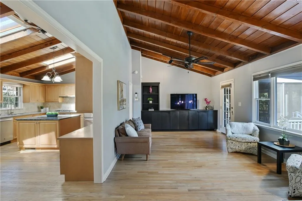 Living room with lofted ceiling with skylight, wooden ceiling, light wood-style flooring, and ceiling fan with notable chandelier