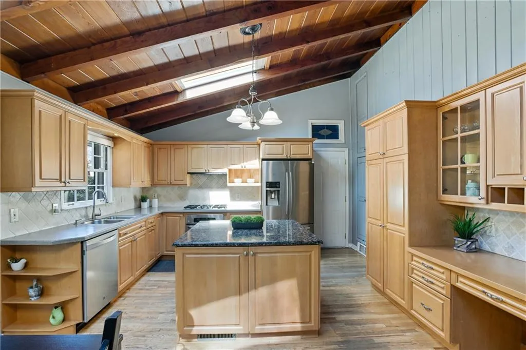 Kitchen with light wood finished floors, appliances with stainless steel finishes, lofted ceiling with skylight, a sink, and a kitchen island