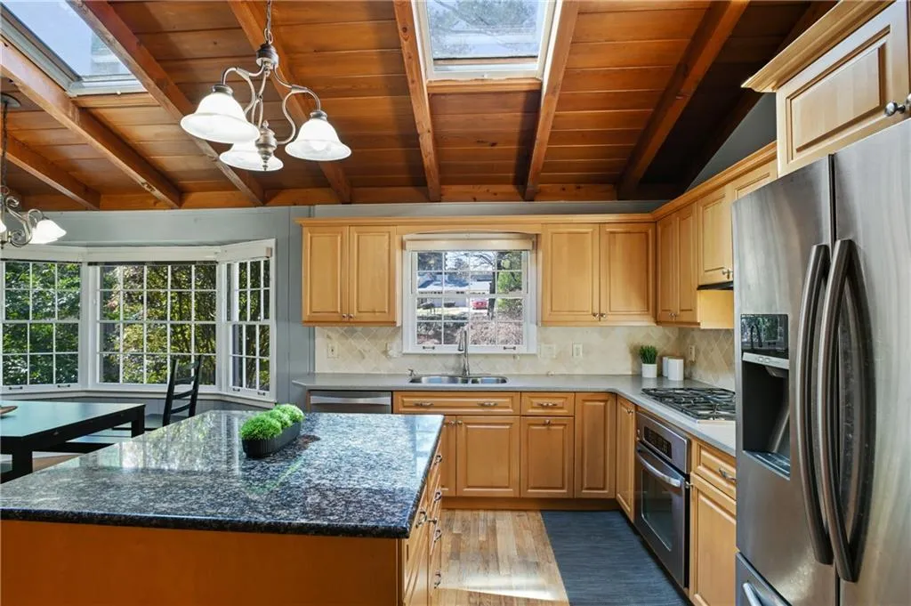 Kitchen with backsplash, appliances with stainless steel finishes, light brown cabinets, a sink, and a chandelier