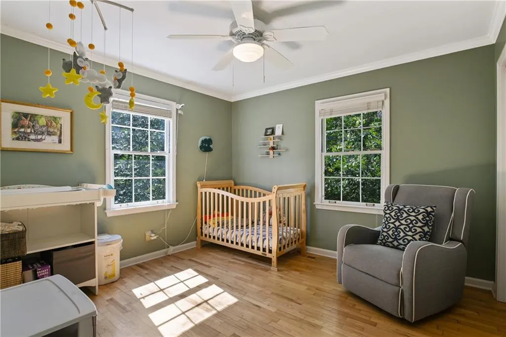 Bedroom featuring light wood-style flooring, multiple windows, ornamental molding, and a crib