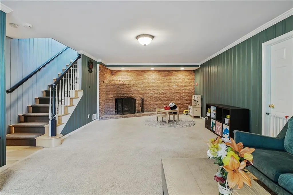 Living area with brick wall, stairway, ornamental molding, carpet floors, and a fireplace