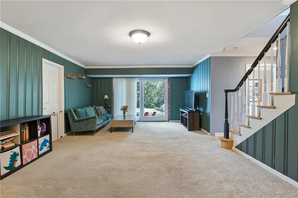Sitting room with ornamental molding, carpet flooring, stairway, and baseboards