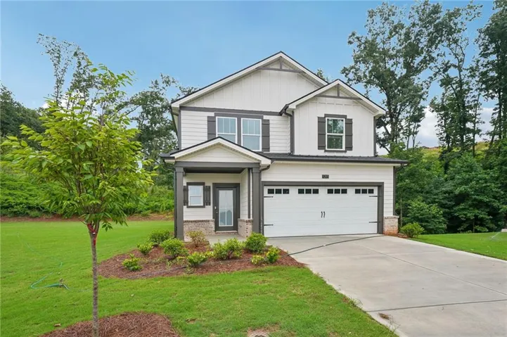 Two-story residence featuring white siding with dark trim accents, a covered entry porch, an attached garage, a paved driveway, and established landscaping