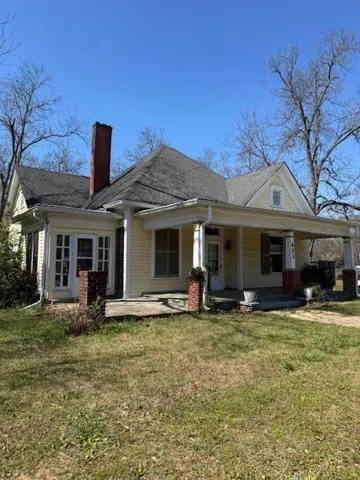 View of front of home with a front yard, covered porch, a chimney, and roof with shingles