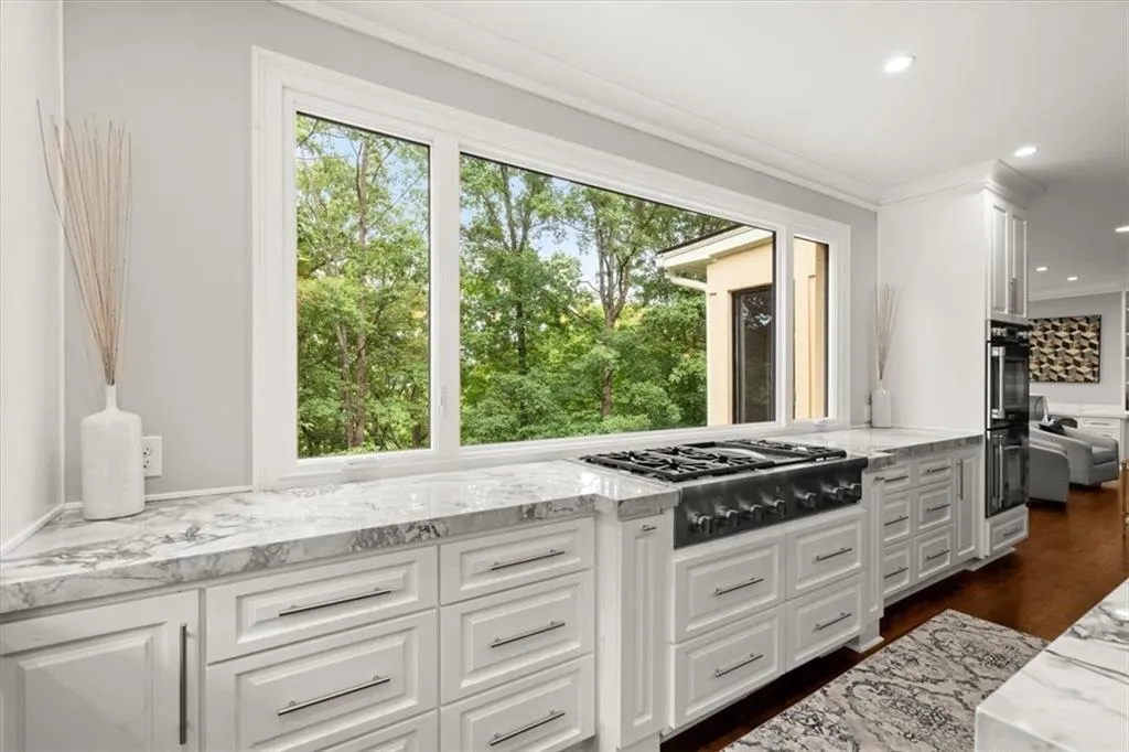 Kitchen featuring white cabinets, light stone countertops, dark hardwood / wood-style floors, and a healthy amount of sunlight Kitchen featuring white cabinets, light stone countertops, dark hardwood / wood-style floors, and a healthy amount of sunlight