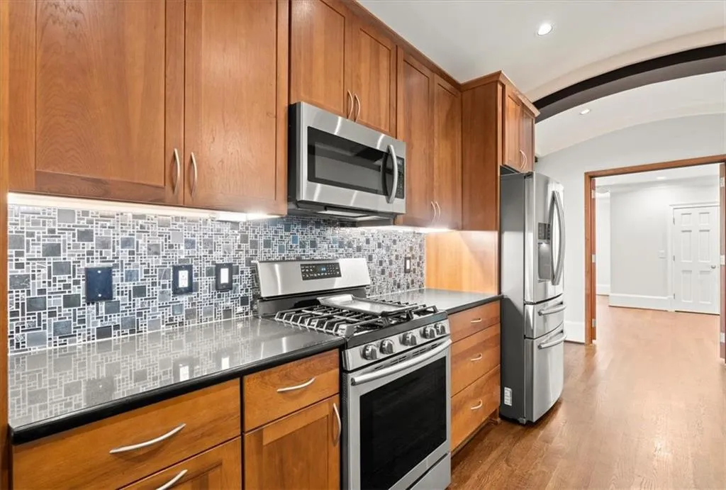 Kitchen featuring dark stone counters, light hardwood / wood-style flooring, tasteful backsplash, and stainless steel appliances Kitchen featuring dark stone counters, light hardwood / wood-style flooring, tasteful backsplash, and stainless steel appliances