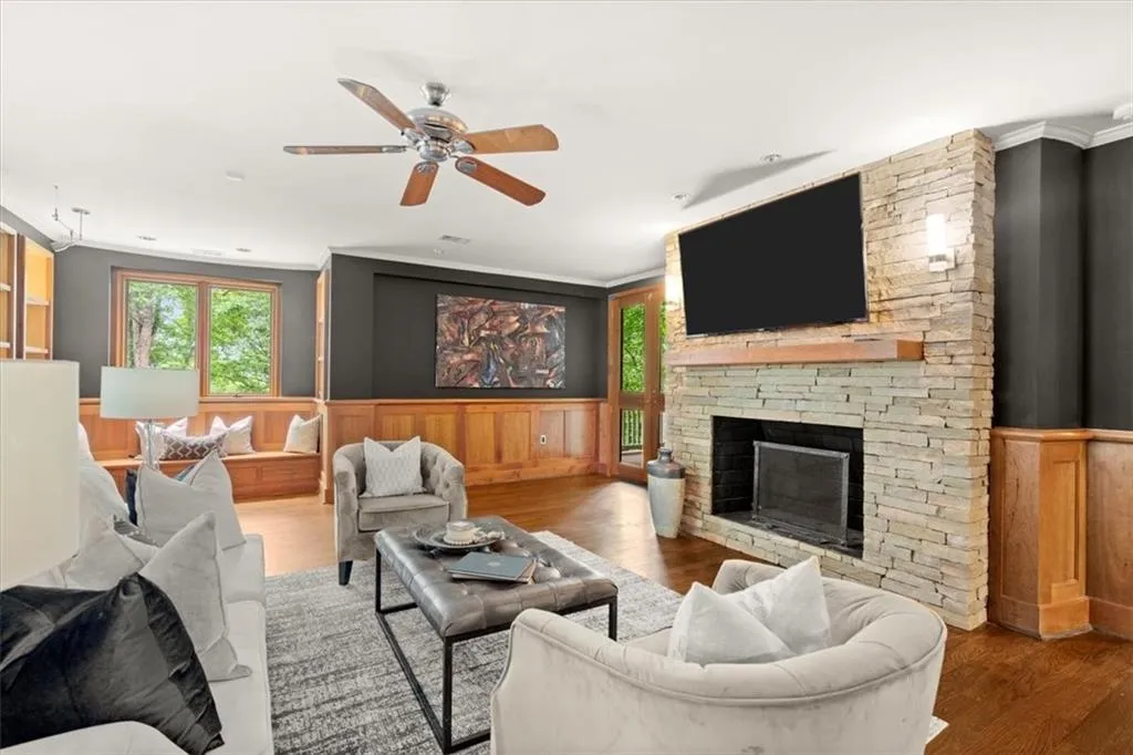 Living room featuring dark wood-type flooring, a stone fireplace, ornamental molding, and ceiling fan Living room featuring dark wood-type flooring, a stone fireplace, ornamental molding, and ceiling fan