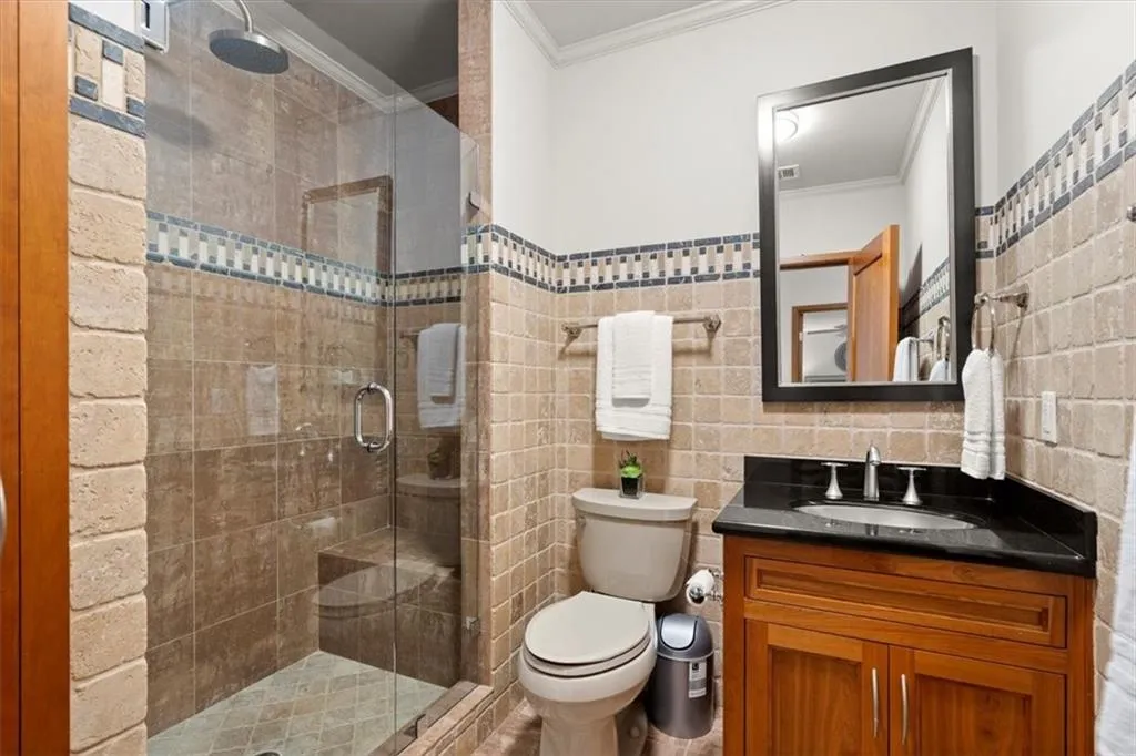 Bathroom with vanity, ornamental molding, tile walls, toilet, and a shower with shower door Bathroom with vanity, ornamental molding, tile walls, toilet, and a shower with shower door