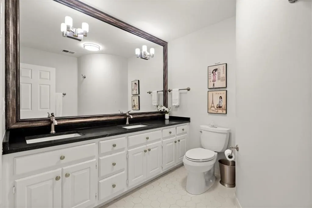 Bathroom with toilet, oversized vanity, dual sinks, a chandelier, and tile flooring Bathroom with toilet, oversized vanity, dual sinks, a chandelier, and tile flooring