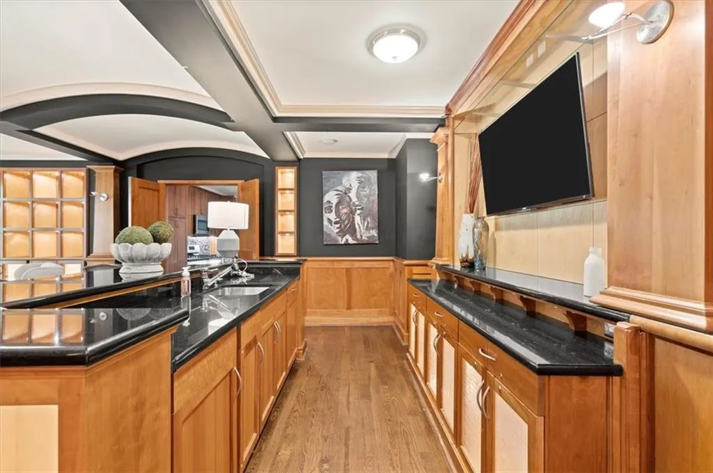 Bar featuring dark stone counters, coffered ceiling, ornamental molding, sink, and hardwood / wood-style floors Bar featuring dark stone counters, coffered ceiling, ornamental molding, sink, and hardwood / wood-style floors
