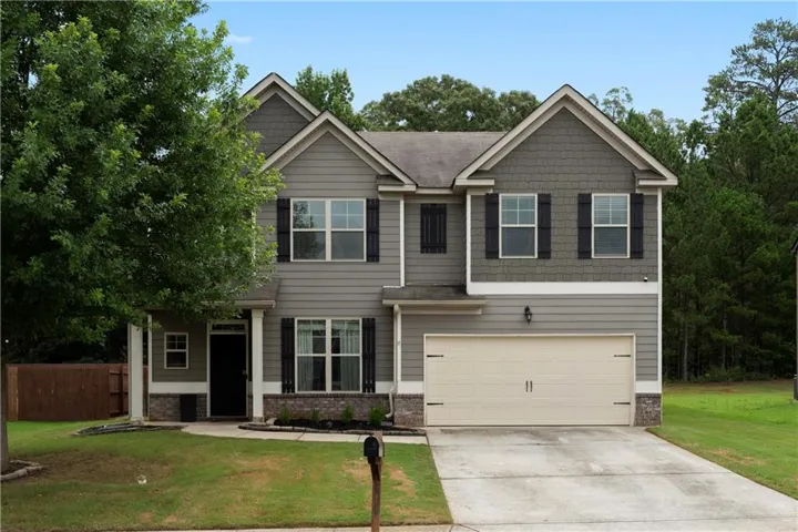 Two-story residence featuring a neutral siding exterior, stone facade accents, an attached two-car garage, and a manicured front lawn
