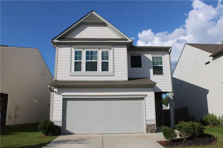 Contemporary two-story residence featuring light-colored siding, a prominent front-facing gable, and an integrated garage with a paneled door