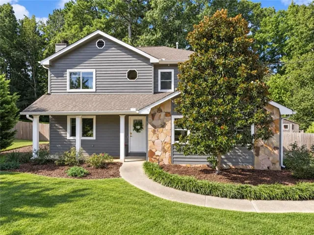 Stone accent siding, mature landscaping, paved walkway, covered entry, and wood siding