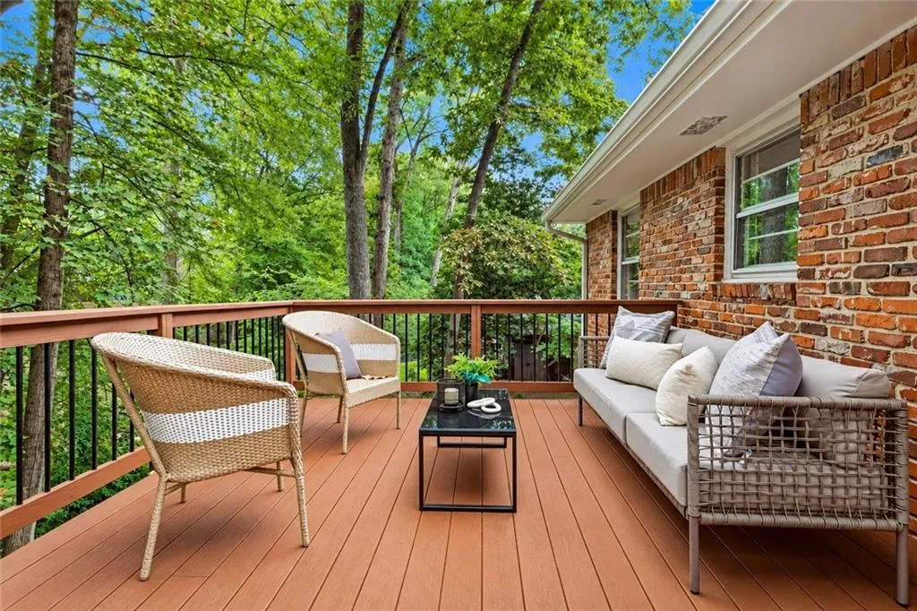 Elevated deck featuring composite wood-finish decking, railings with vertical metal balusters, brick exterior wall, and mature tree canopy