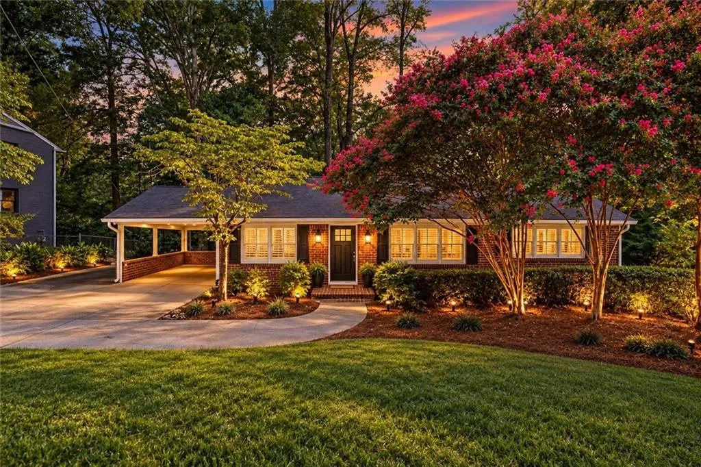 Brick exterior facade featuring a covered carport, multi-pane windows, mature landscaping, and an asphalt driveway