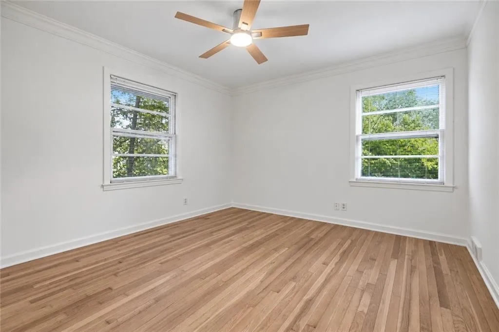 Wood-finish flooring, crown molding, dual double-hung windows, and a ceiling fan with integrated lighting