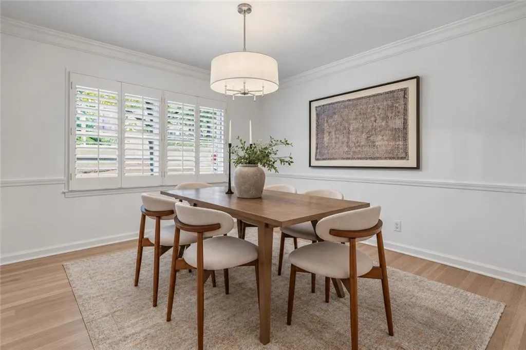 Room featuring wood-finish flooring, plantation shutters, crown molding, chair rail trim, and a drum pendant light fixture
