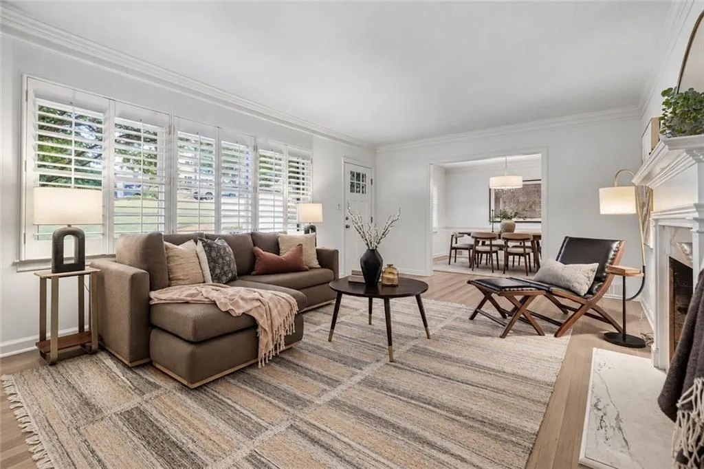 Living area featuring wood-finish flooring, plantation shutters, crown molding, and a fireplace with a white mantel