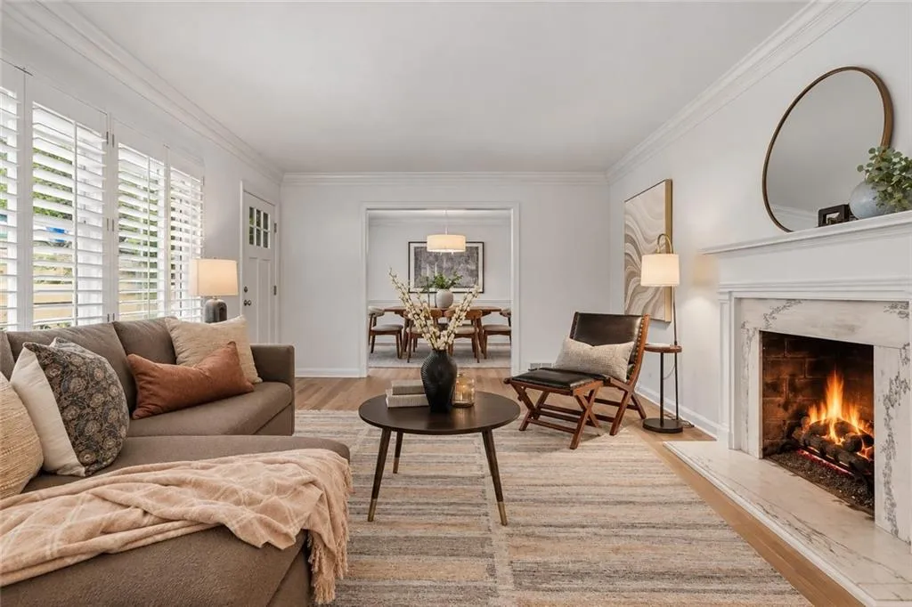 Living area featuring a fireplace with a stone-surround mantel, wood-finish flooring, plantation shutters, and crown molding