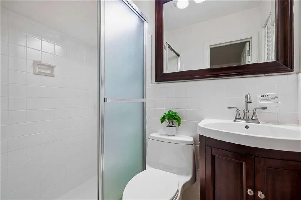Bathroom featuring a dark wood-finish vanity, white sink with a dual-handle faucet, integrated wall mirror, and a tiled shower enclosure with a frosted glass door