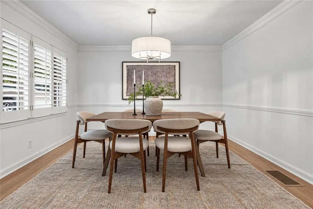 Dining area featuring wood-finish flooring, white chair rail molding, crown molding, plantation shutters, and a central drum pendant light fixture