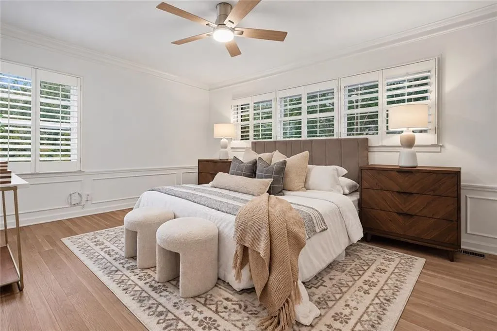 Room featuring wood-finish flooring, wainscoting, white plantation shutters, and a central ceiling fan with integrated lighting