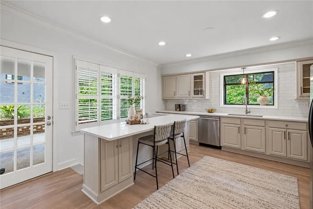 Kitchen featuring a quartz countertop island, custom shaker-style cabinetry, subway tile backsplash, stainless steel dishwasher, and wood-finish flooring
