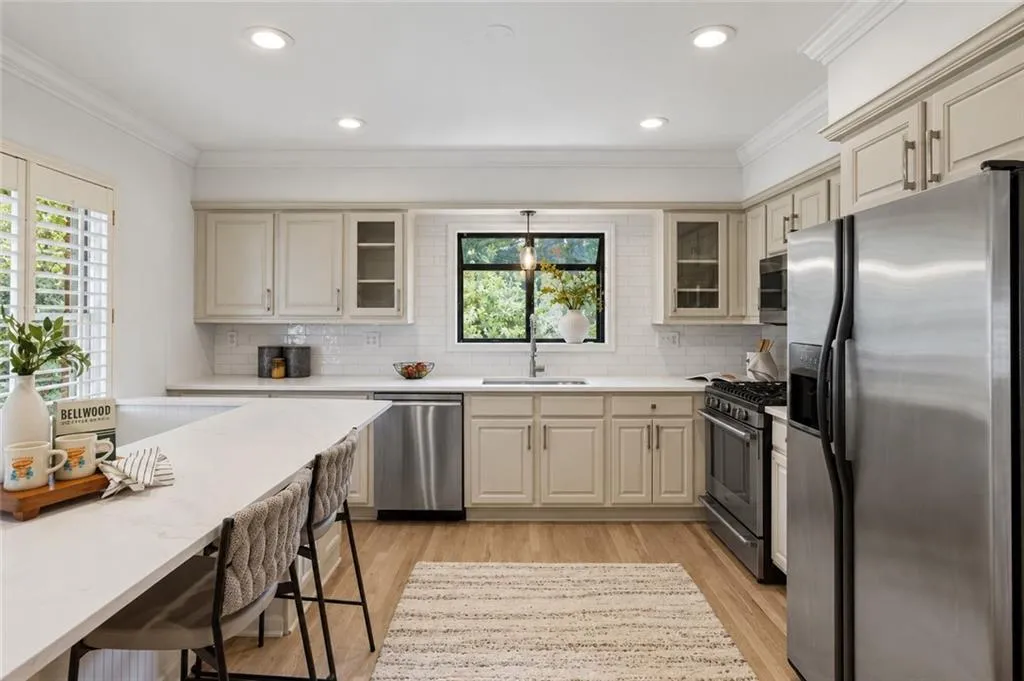 Kitchen featuring neutral-toned cabinetry, solid surface countertops, a white subway tile backsplash, stainless steel appliances, and wood-finish flooring