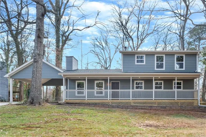 View of front of property featuring covered porch, a front yard, a chimney, and an attached carport