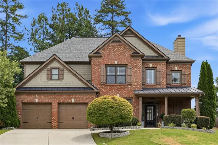 Brick facade residence featuring a covered front entry with columns, a two-car garage with carriage-style doors, multiple gables, and decorative window shutters