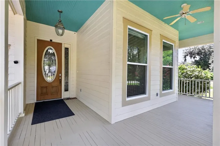 Covered front porch with a wood-panel ceiling, decorative ceiling fan, and a wood entry door with an oval-shaped glass insert