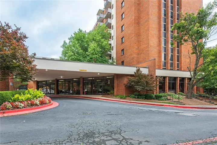 Brick facade with a covered entrance, expansive windows, mature trees, and landscaped grounds