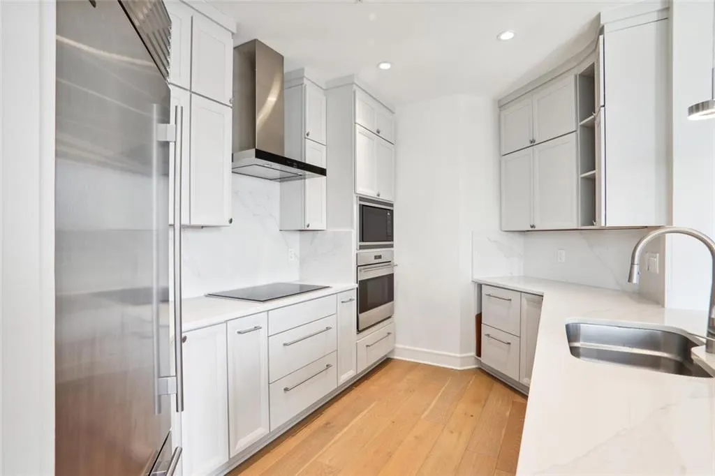 Kitchen with light wood-style flooring, wall chimney range hood, black appliances, open shelves, and a sink