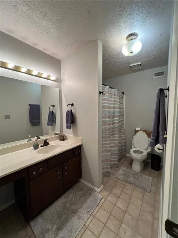 Bathroom with toilet, tile floors, vanity, and a textured ceiling