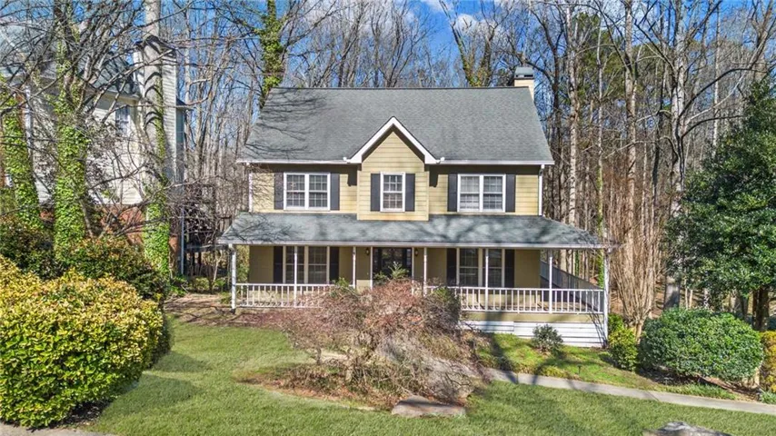 View of front of house with a chimney, a porch, roof with shingles, and a front lawn