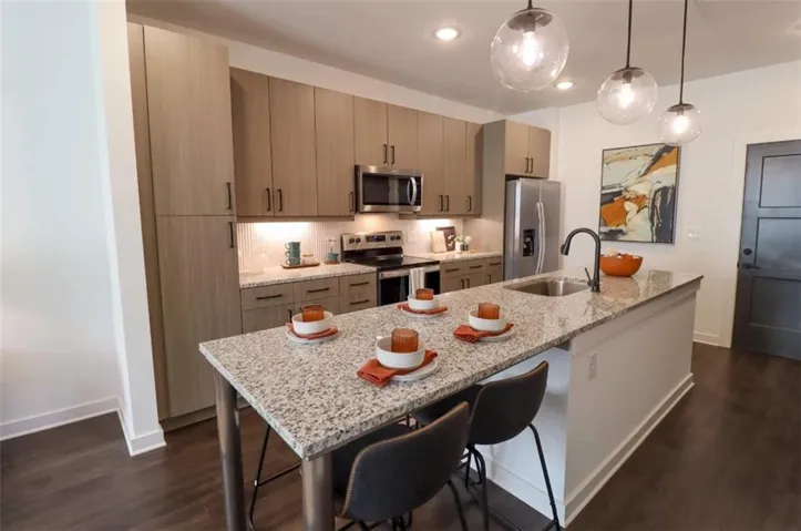 Kitchen featuring light stone counters, appliances with stainless steel finishes, an island with sink, pendant lighting, and a breakfast bar area