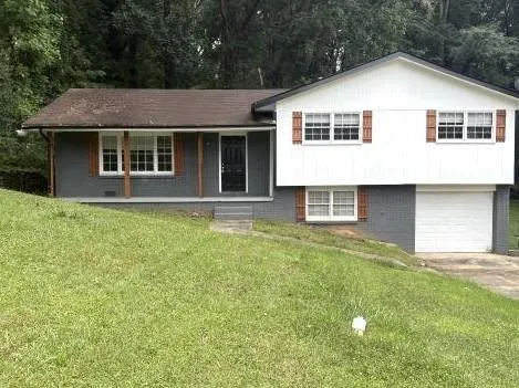 Split-level residence featuring a white garage door, white siding, and gray brickwork