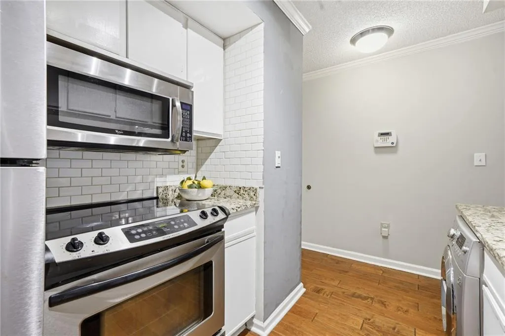 Kitchen featuring stainless steel appliances, crown molding, white cabinets, a textured ceiling, and light wood-style flooring