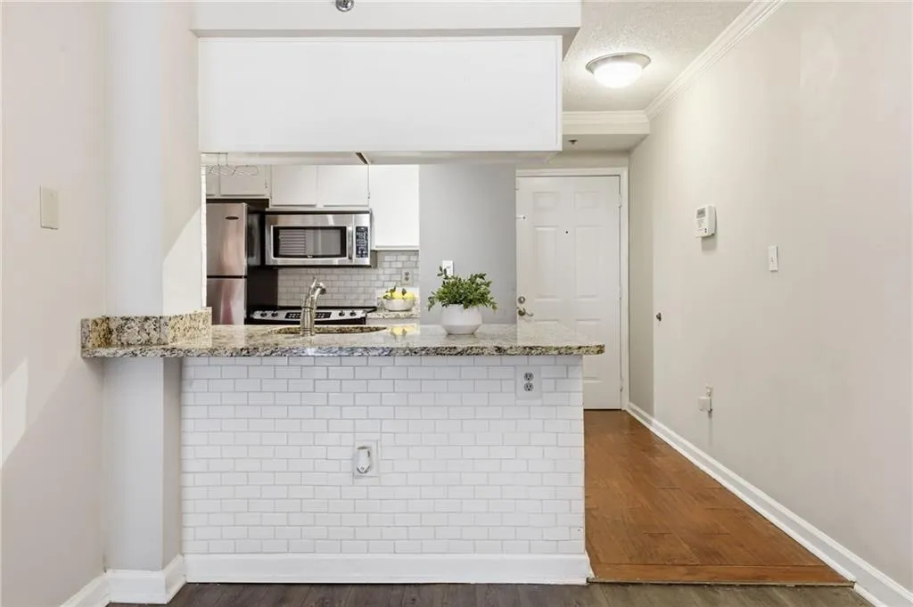 Kitchen featuring light stone countertops, a peninsula, a textured ceiling, white cabinets, and decorative backsplash