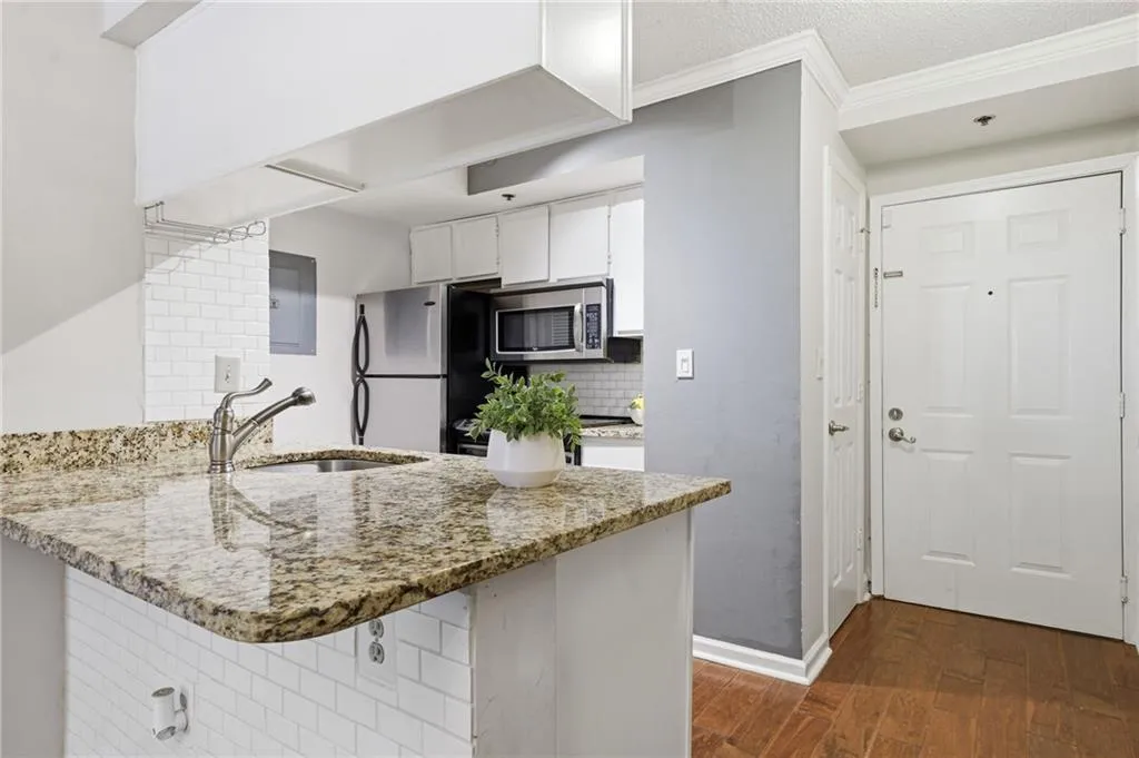 Kitchen with a peninsula, white cabinets, dark wood-style flooring, light stone countertops, and stainless steel appliances