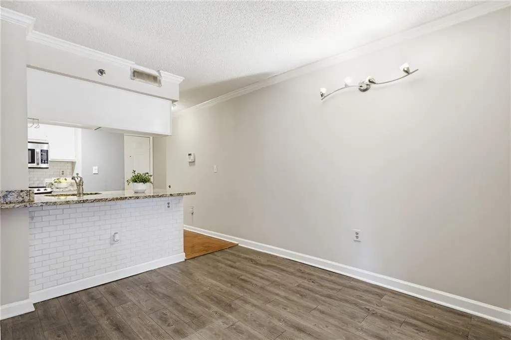 Kitchen featuring ornamental molding, dark wood-style flooring, light stone countertops, a peninsula, and backsplash