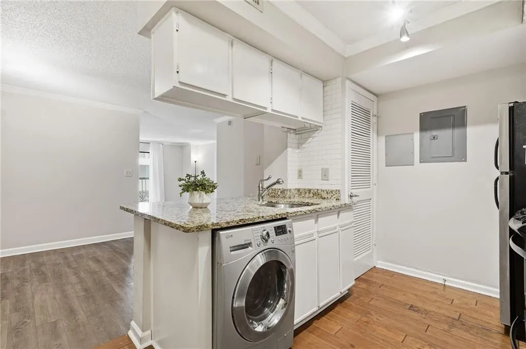 Kitchen featuring washer / dryer, white cabinets, crown molding, electric panel, and light wood finished floors