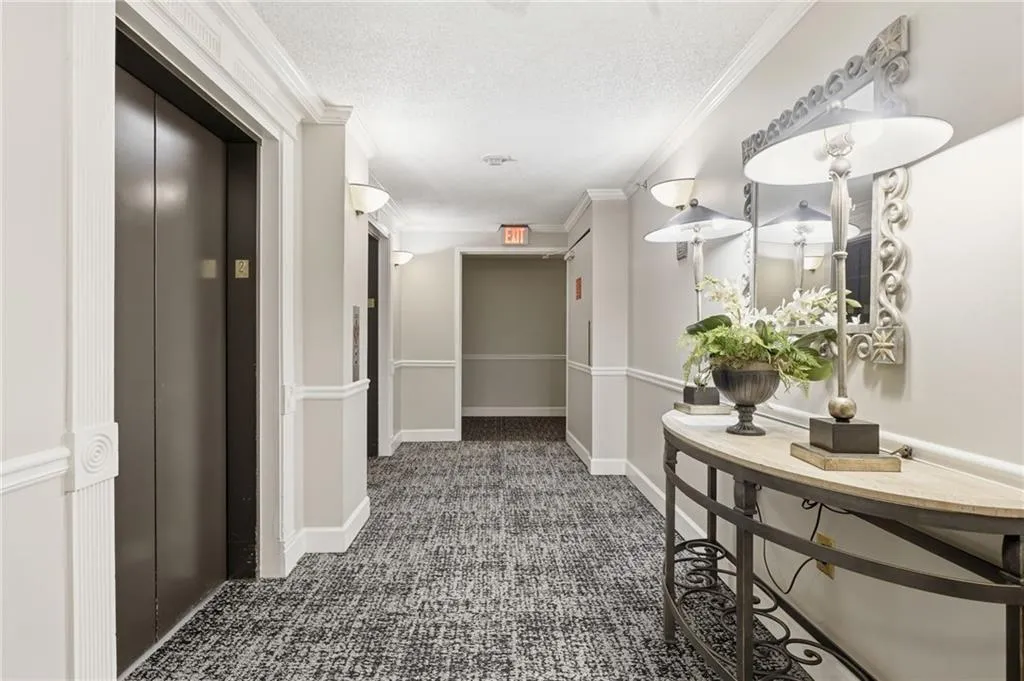 Corridor featuring dark colored carpet, elevator, crown molding, and a textured ceiling