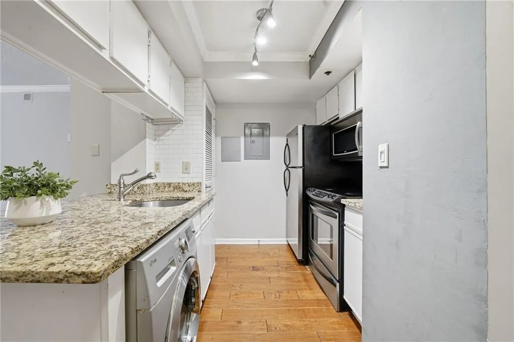 Kitchen featuring crown molding, white cabinetry, washer / clothes dryer, light stone counters, and stainless steel appliances