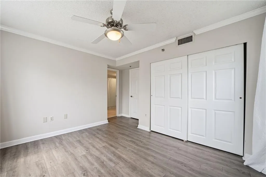 Unfurnished bedroom featuring ornamental molding, a textured ceiling, ceiling fan, light wood-style floors, and a closet
